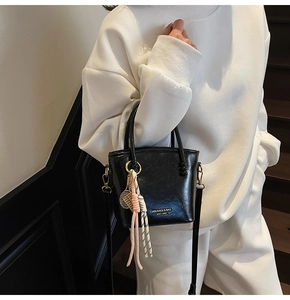 Detail of black contrast bucket bag with tennis racket charm and gold brand plate