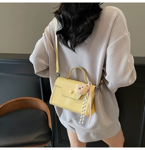 Close-up of yellow leather crossbody bag with teddy bear charm and striped ribbon detail
