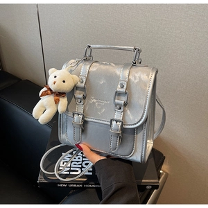 Detail of silver metallic backpack featuring vintage buckles and a cute bear charm
