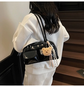 Detailansicht einer schwarzen glänzenden Umhängetasche mit Bärenanhänger auf weißem Outfit