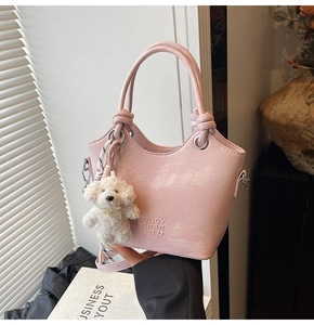 Détail du sac seau rose clair avec bord ondulé, poignée en cuir et breloque ours en peluche