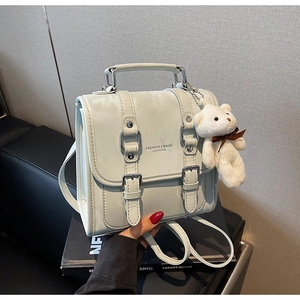 Detail view of mint green leather backpack with silver buckles and plush bear charm