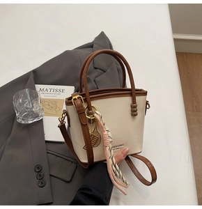 Detail of cream and brown bucket bag with woven pendant on grey blazer background
