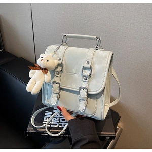 Detail of light green faux leather bag with decorative buckles and a cute bear charm