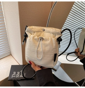 Detail of a creamy white quilted bucket bag featuring a silver snap and black cord strap