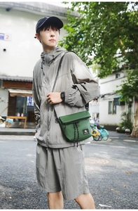 Outdoor street shot of a dark green nylon messenger bag with black logo and drawstring detail