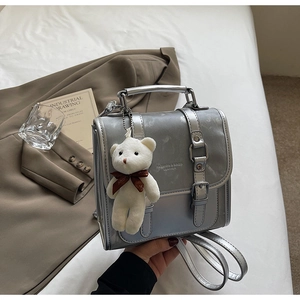 Detail of silver gray leather backpack featuring plush bear charm and fashion text