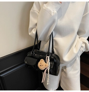 Detail der schwarzen Lackleder-Tasche mit zwei Klappentaschen und süßem Bärenanhänger
