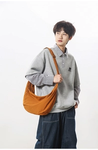 Detailed view of the large orange crescent crossbody bag worn with a gray hoodie