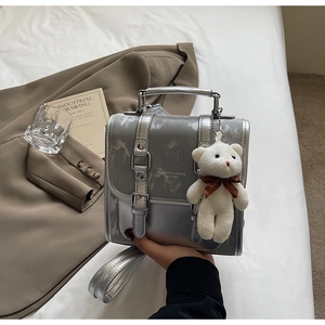 Detail of silver metallic backpack with decorative buckles and plush bear charm
