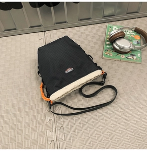 Detail of crossbody bag showing black ripstop nylon grid texture and orange cord