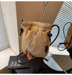 Detail of khaki drawstring crossbody bucket bag showing nylon material and metal magnetic snap