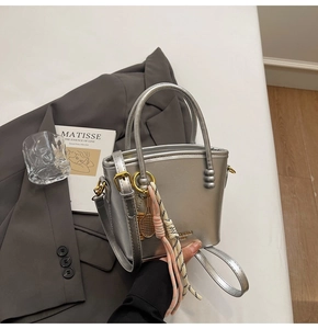 Detail of silver metallic bucket bag with dual handles and woven tassel charm