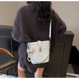 Detail of light gray bucket bag with glossy leather and pearl bow charm on shoulder