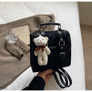 Detail of black faux leather backpack with silver buckle and plush bear pendant accessory