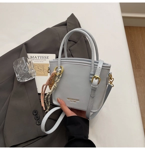 Detail view of the light blue leather bucket bag with gold lettering and woven charm
