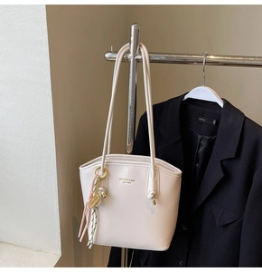 Dettaglio della borsa a secchiello in pelle beige con logo e ciondolo a nastro a righe