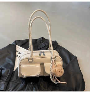 Detail der weißen Boston Tasche mit Doppelgriffen und braunem Plüschbären auf schwarzer Jacke