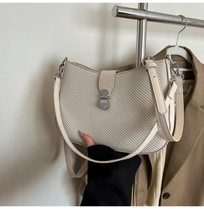Detail of the woven texture and silver metal push-lock on the cream shoulder bag