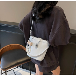 Detail of light gray bucket bag featuring silver lock and pearl bow charm accessory