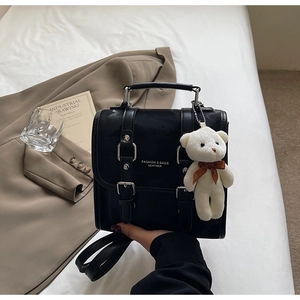 Close-up of black leather backpack with dual buckles and a cute white plush bear charm