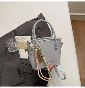 Close-up of light blue leather bucket bag featuring gold tennis racket charm and brand logo