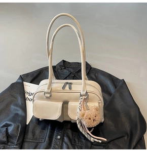 Detail einer cremefarbenen Leder-Boston-Tasche mit Fronttaschen und Bärenanhänger
