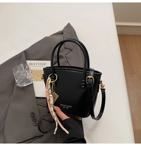 Detail of black glossy handbag with twin handles and golden abacus charm