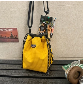 Detail view of yellow plaid drawstring bucket bag with adjustable nylon strap and logo