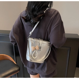 Detail of silver metallic bucket bag with plaid bow and pearl charm worn on shoulder