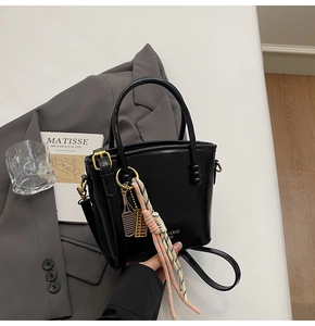 Detail of black glossy bucket bag featuring gold hardware and unique tennis racket charm