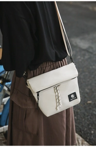 Detail of off-white nylon crossbody bag with black zipper and decorative drawstring