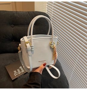 Detail of light blue bucket bag with gold lettering and decorative silk scarf accessory