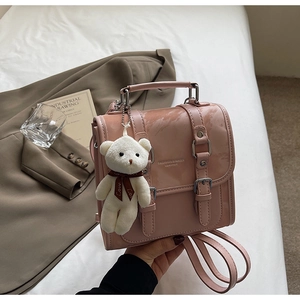 Detailed view of pink glossy backpack with metal buckles and plush bear charm