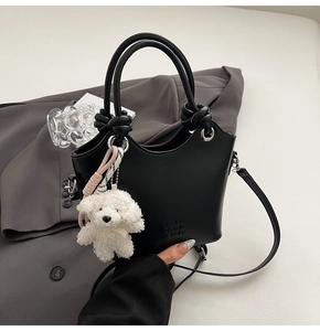 Détail d'un sac seau en cuir noir avec poignées rondes et charmant pendentif chien en peluche