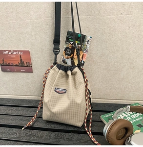 Close-up of beige checkered drawstring bucket bag with branded label and woven rope detail