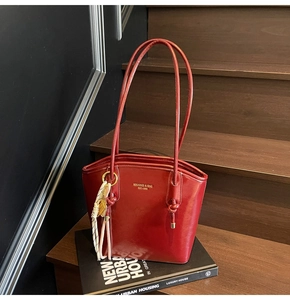 Dettaglio della borsa tote in pelle lucida bordeaux con logo dorato e nappa decorativa