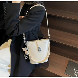 Vista dettagliata di una borsa a secchiello in pelle bianco crema con ciondolo a perla