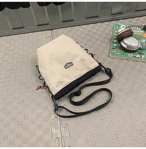 Detail of grid patterned crossbody bag with drawstring closure and adjustable strap