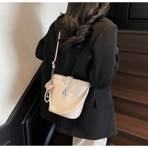 Detail of glossy cream bucket bag with decorative pearl and heart charm pendant