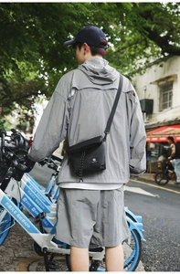Outdoor street view of a black nylon crossbody bag worn on a gray techwear outfit