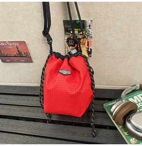 Close-up of red plaid bucket bag with black drawstrings and branded label on canvas fabric