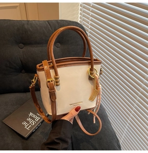 Detail of cream and brown bucket bag with gold lettering, silk scarf and metal charm