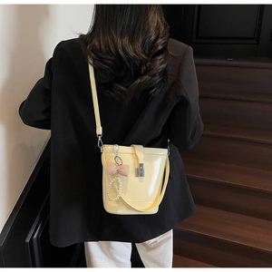 Detail of yellow glossy bucket bag with pearl and checkered bow charm on wooden stairs