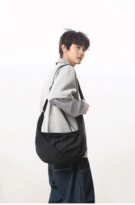 Side view of black nylon crescent crossbody bag worn by model on white background