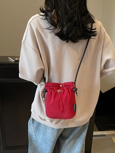 Minimalist red drawstring crossbody phone bag with black leather strap and brand label