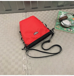 Flat lay of red and black checkered drawstring bucket bag with adjustable strap and headphones