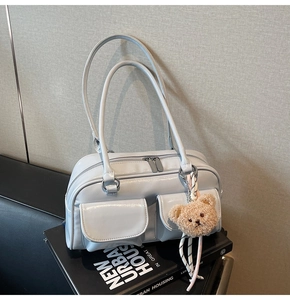 Detail der hellblauen glänzenden Boston-Tasche mit Klappentaschen und Bärenanhänger