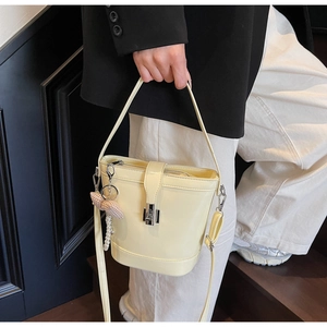 Detail view of cream bucket bag with glossy finish, bow charm and pearl pendant detail