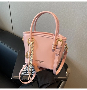 Detailed view of pink crossbody bucket bag with branding and woven rope pendant